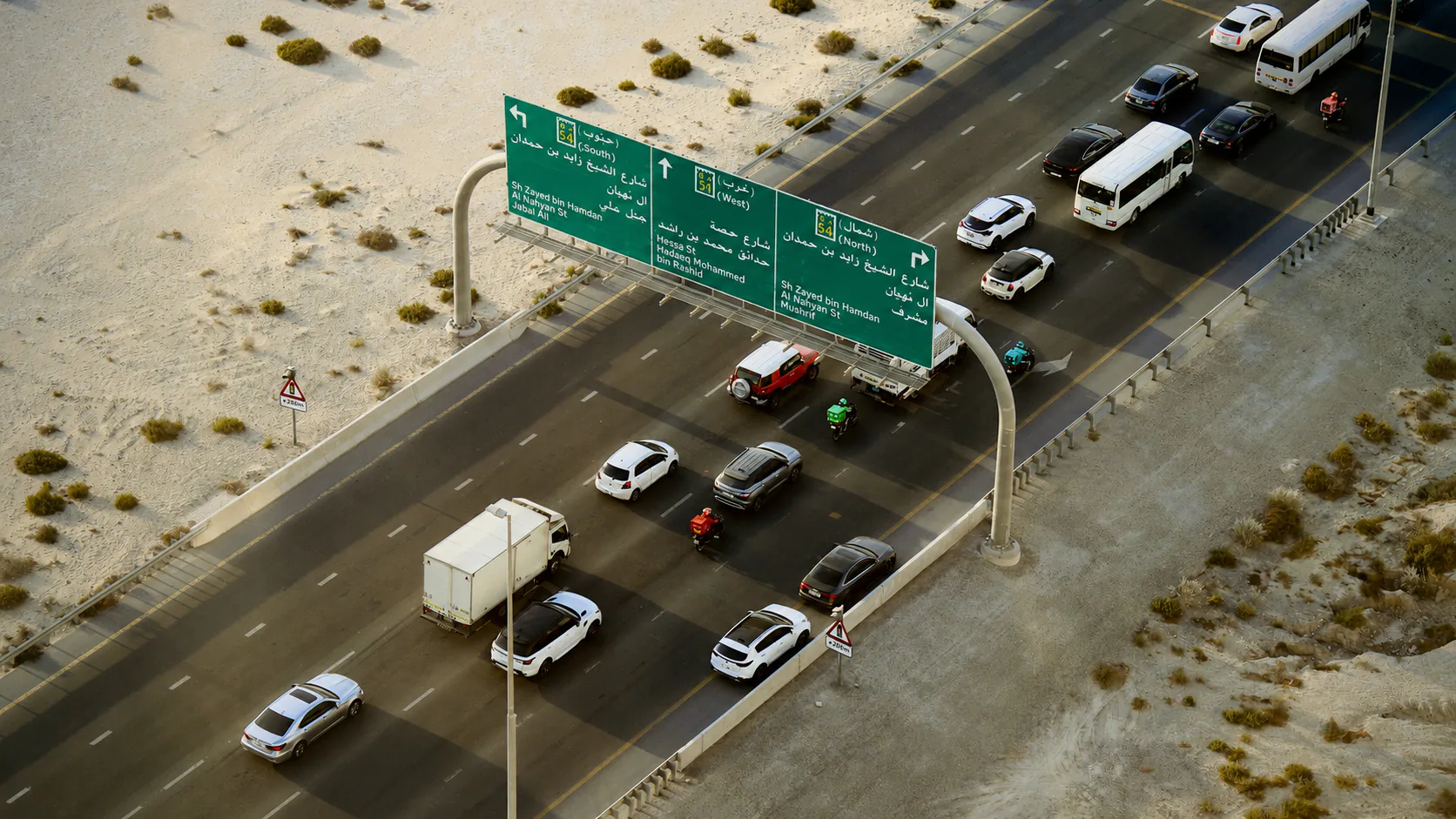 UAE highway traffic passing beneath bilingual directional signs
